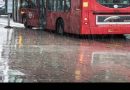 Heavy rain on city street with red bus and water reflection